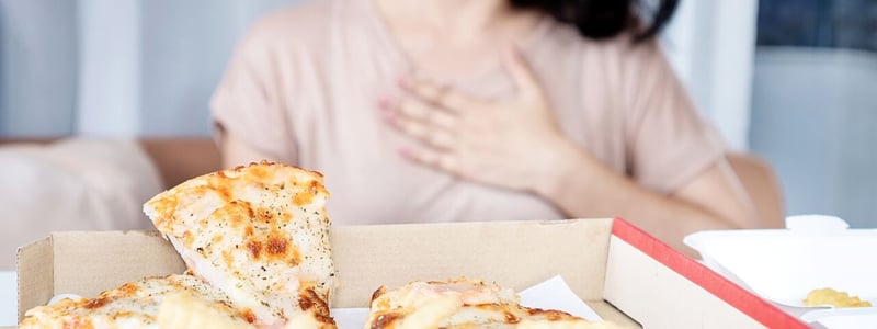 Frau hält sich die Hand an das Brustbein, nachdem sie Pizza und Pommes gegessen hat.
