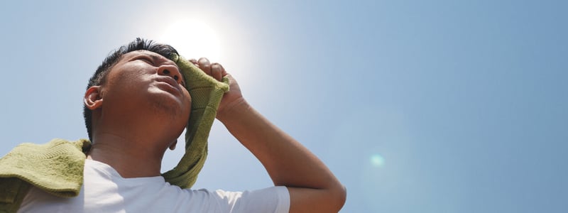 Mann trocknet schwitzendes Gesicht mit grünem Handtuch in der prallen Sonne