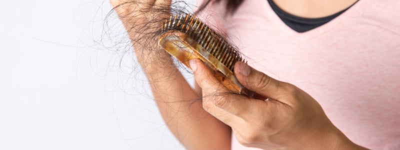 Es ist der Oberkörper und die Hände einer Frau zu sehen. Sie hält eine Bürste in der Hand in der sich ein Haarbüschel befindet.