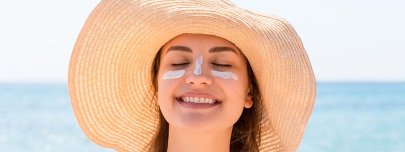 Junge Frau am Meer, die einen Sonnenhut trägt und Sonnencreme im Gesicht hat.