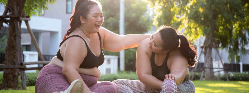 Zwei Übergewichtige Frauen machen Yoga-Übungen im Park und haben Spaß dabei.