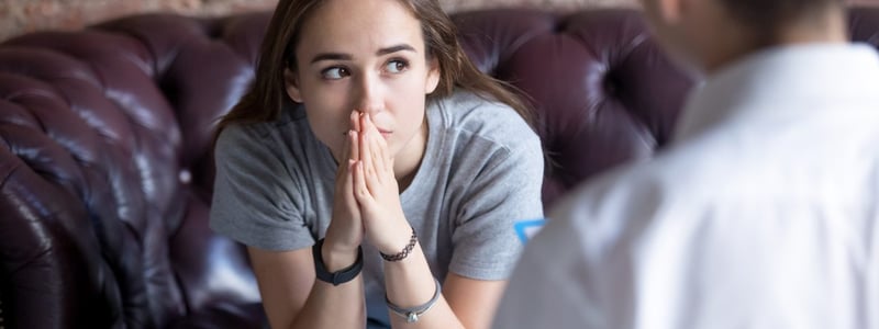 Mädchen sitzt auf einer Ledercouch, sie guckt besorgt. Vor ihr sitzt eine Psychotherapeutin.