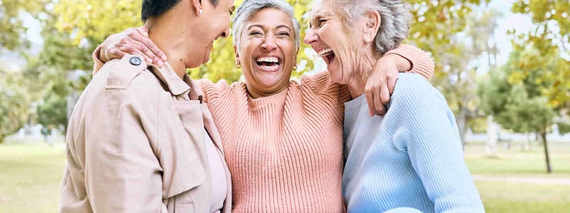 Drei ältere Frauen lachen im Park.