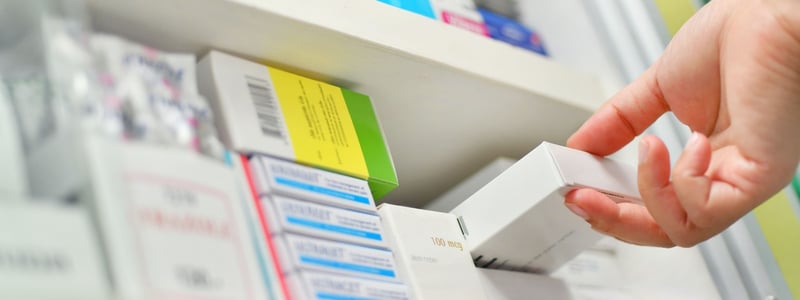 Apotheker oder Apothekerin nimmt Tabletten in Schachtel aus einem Regal.