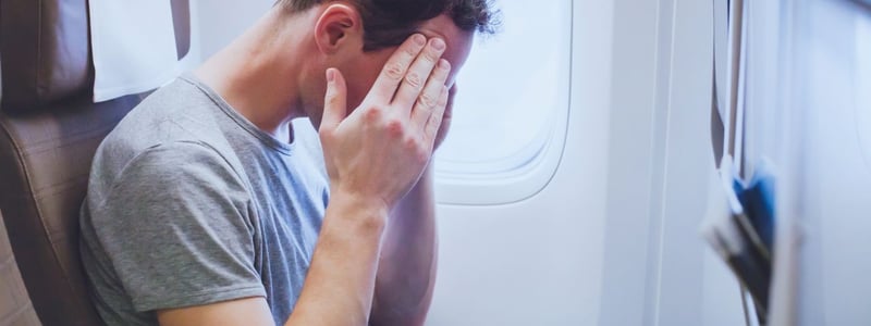 Mann sitzt im Flugzeug und hält sich die Hände vor das Gesicht.