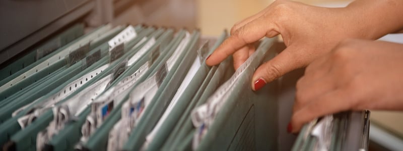 Frauenhände blättern durch Patientenakten in einem Hängeregister.