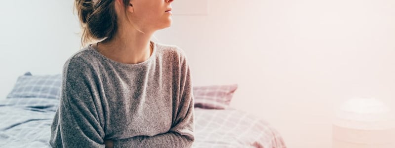 Eine Frau sitzt auf dem Bett und hält sich vor Schmerzen den Bauch.