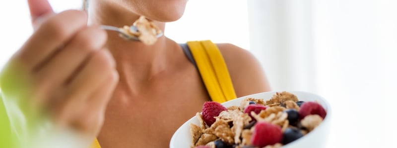 Eine junge Frau im gelben Top ist Müsli mit Beeren.