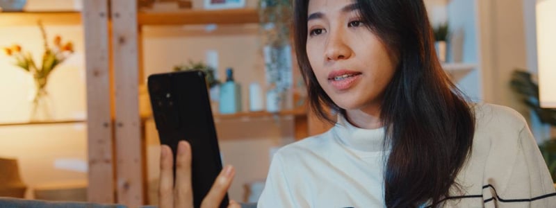Junge Frau hält Smartphone in der Hand und führt ein Videotelefonat.
