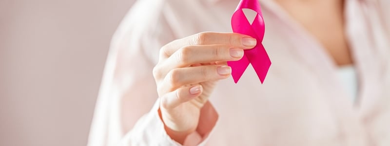 Frau hält rosa Schleife als Zeichen gegen Brustkrebs in der Hand.