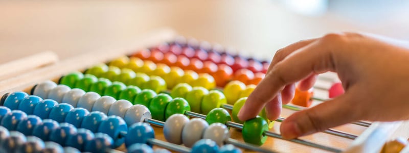 Eine Hand schiebt bunte Perlen zur Berechnung mithilfe eines Abakus hin und her.