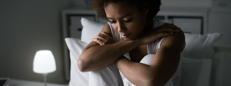 Eine junge Frau sitzt niedergeschlagen auf einem Bett.