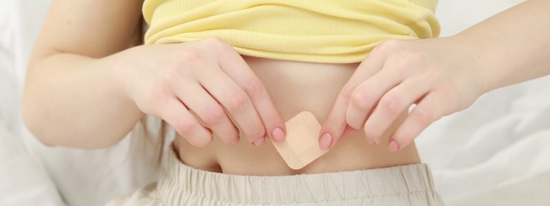 Eine Frau klebt sich ein Pflaster zur Empfängnisverhütung auf den Bauch.