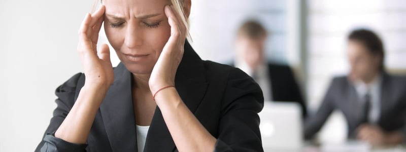 Eine Frau sitzt im Büro und hält sich die Schläfen während eines schmerzhaften Migräneanfalls.