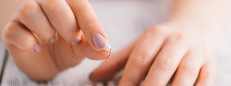 Weibliche Hand hält eine kleine runde Pille.
