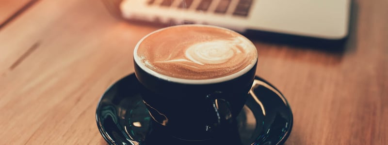 Tasse mit Kaffee neben einem Laptop auf einem Holztisch.