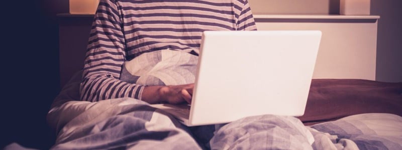 Glücklicher Mann mit Laptop im Bett.